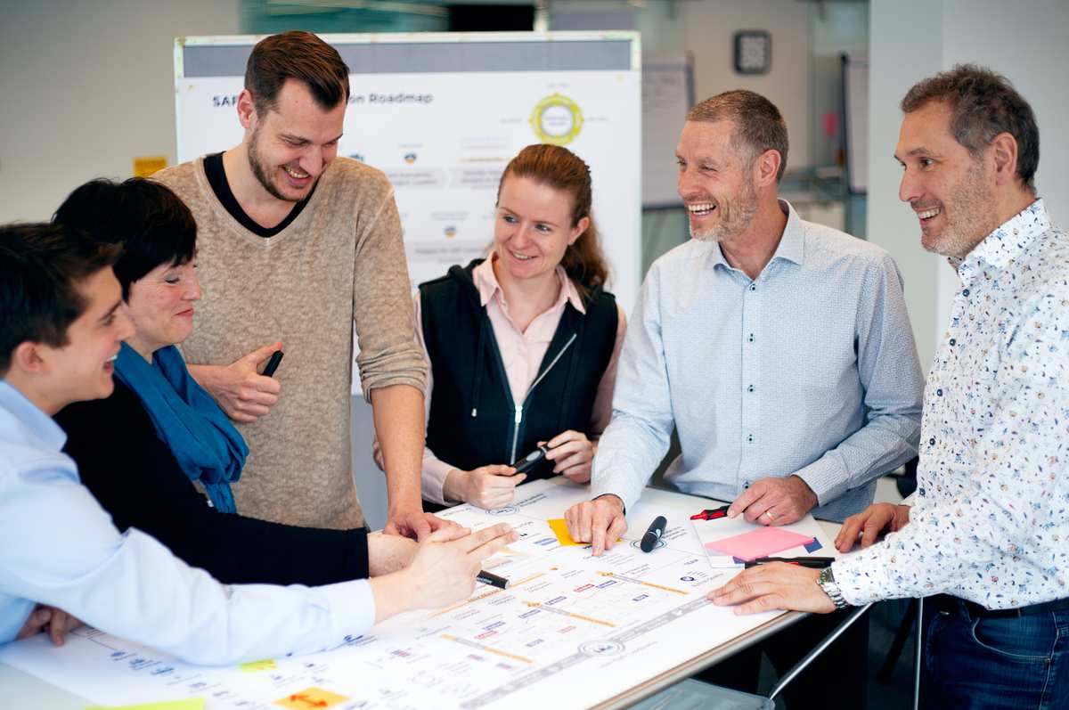 Ein Team arbeitet an einem Tisch vor einem Scaled Agile Poster